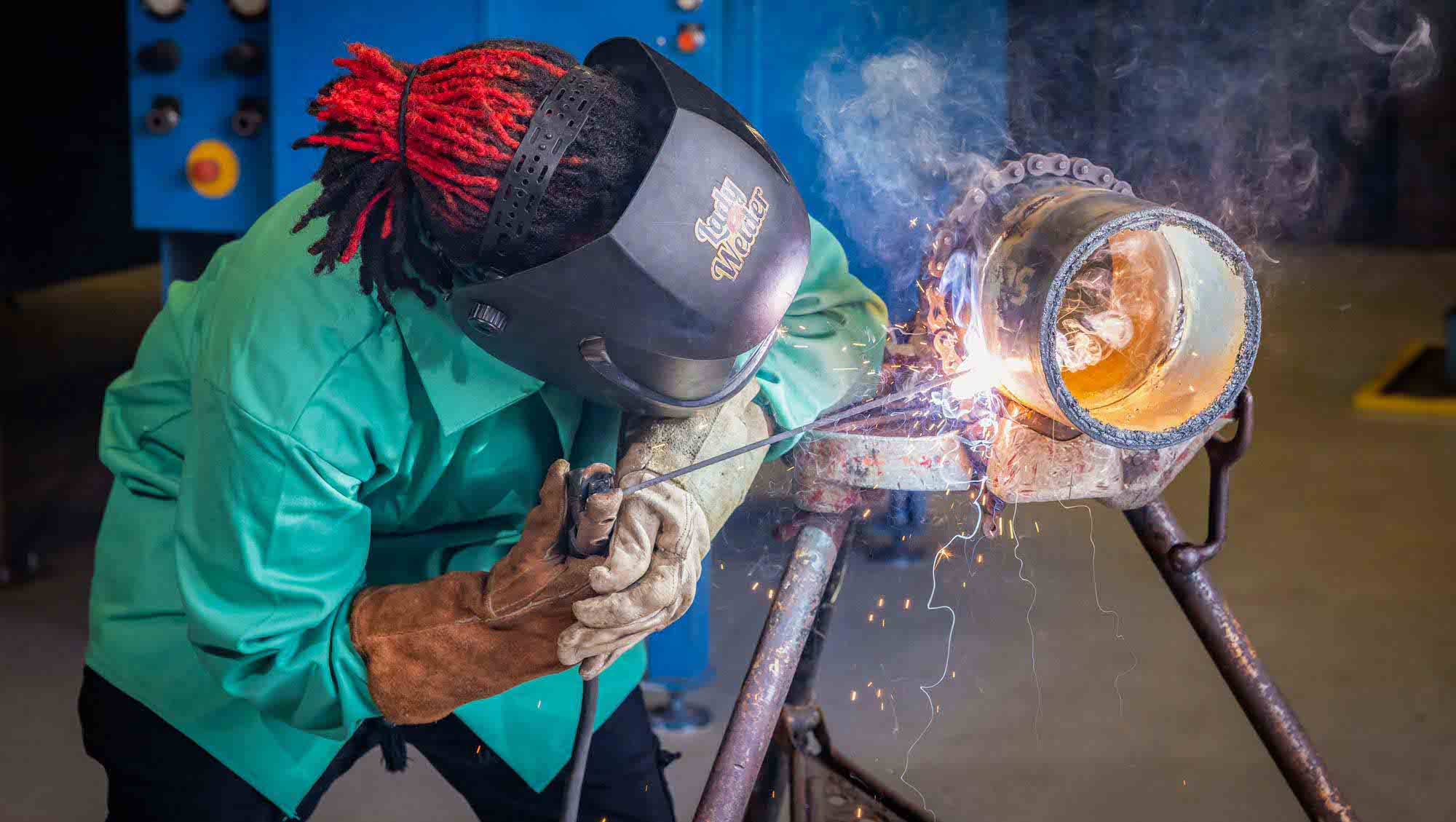 Female welding student welding a pipe together with sparks flying.
