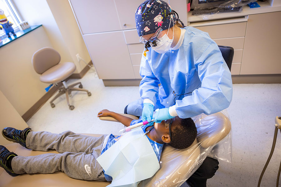 A photo of a child in a dentists chair with a dental hygienist cleaning his teeth