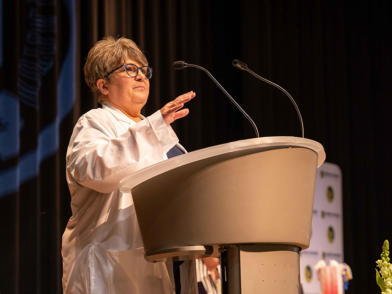 Marianne Caviston is seen standing behind a podium giving a speech.