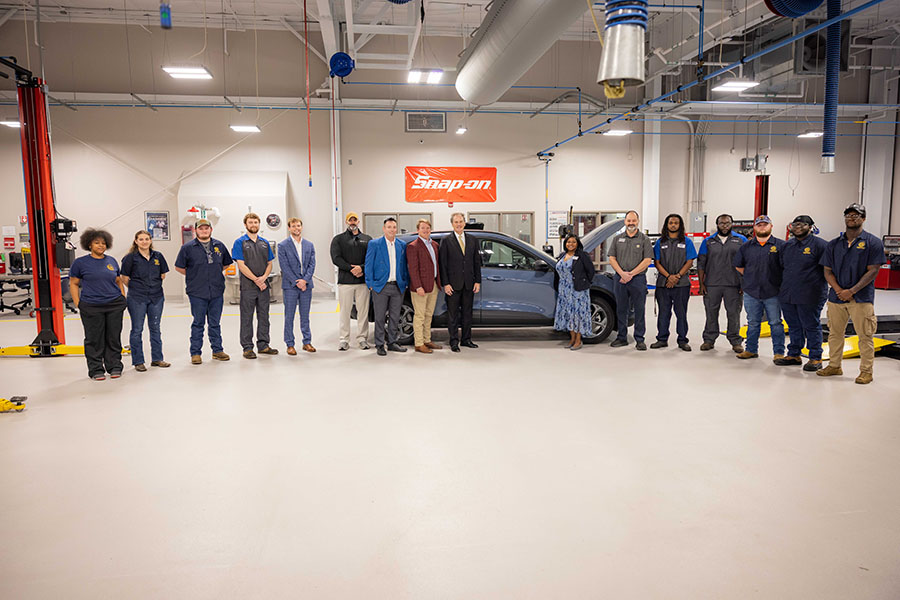 A group of people stand around a car inside of a large room.