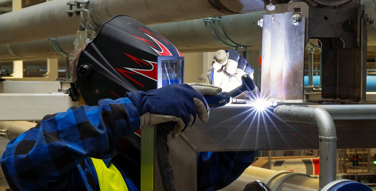 A welder is welding pipe in a manufacturing setting