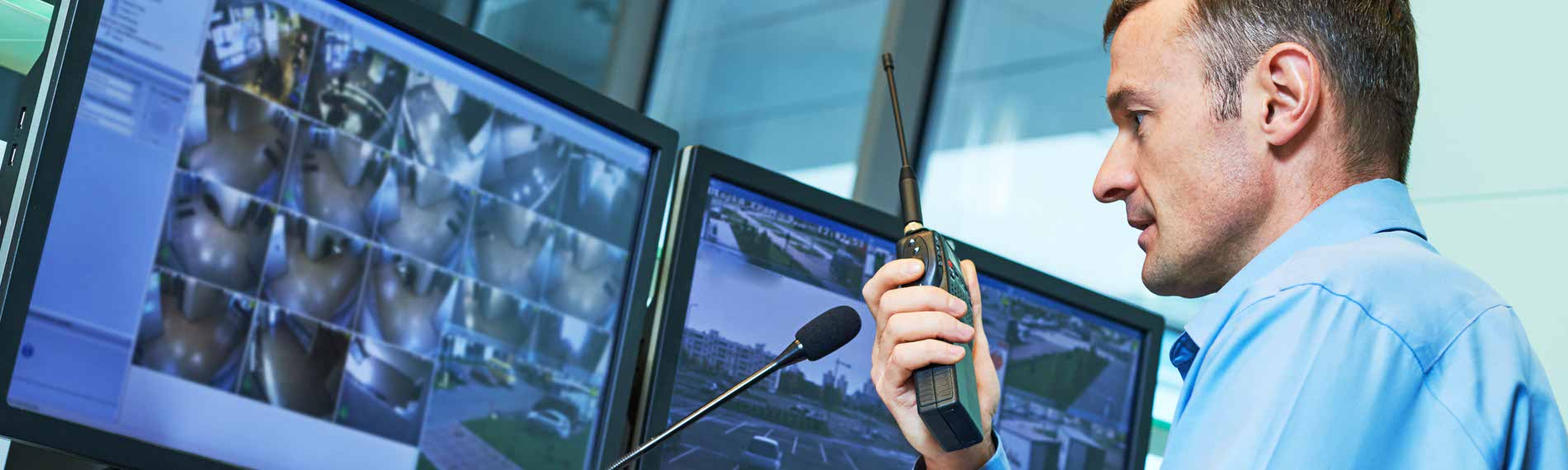 A security officer talks into a radio in front of a cctv display.